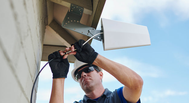Installer mounting a directional outside antenna for a cell phone signal booster under a home's roof eave
