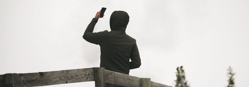 Person on a wooden deck holding a phone overhead to search for cell signal under an overcast sky