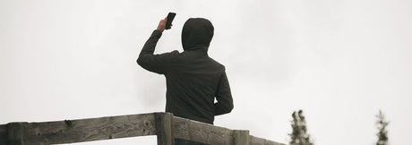 Person on a wooden deck holding a phone overhead to search for cell signal under an overcast sky